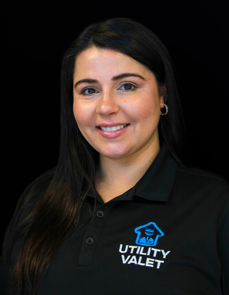 A woman with long dark hair, wearing a black Utility Valet polo shirt, poses against a plain black background.